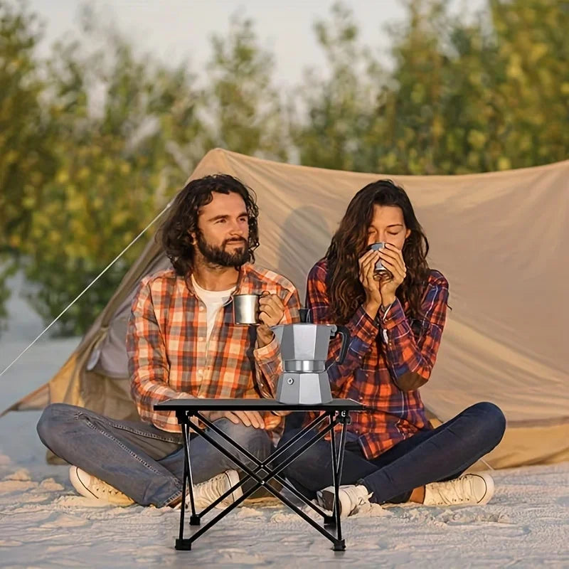 Roll-Up Camping Table at a tent-side coffee break, with two adults sitting behind the small table.