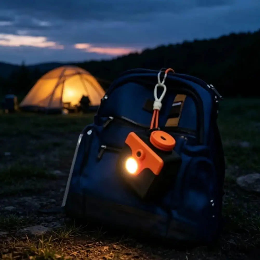 Saltwater Emergency Light clipped to a blue backpack at a campsite with an illuminated tent behind