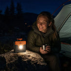 Saltwater Emergency Light glowing on a rock beside a seated camper and tent at night