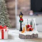 Angled view of Santa Swing Christmas Scene on a table beside a white gift with red ribbon