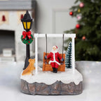 Santa Swing Christmas Scene on a white table with a Christmas tree and fireplace in the background