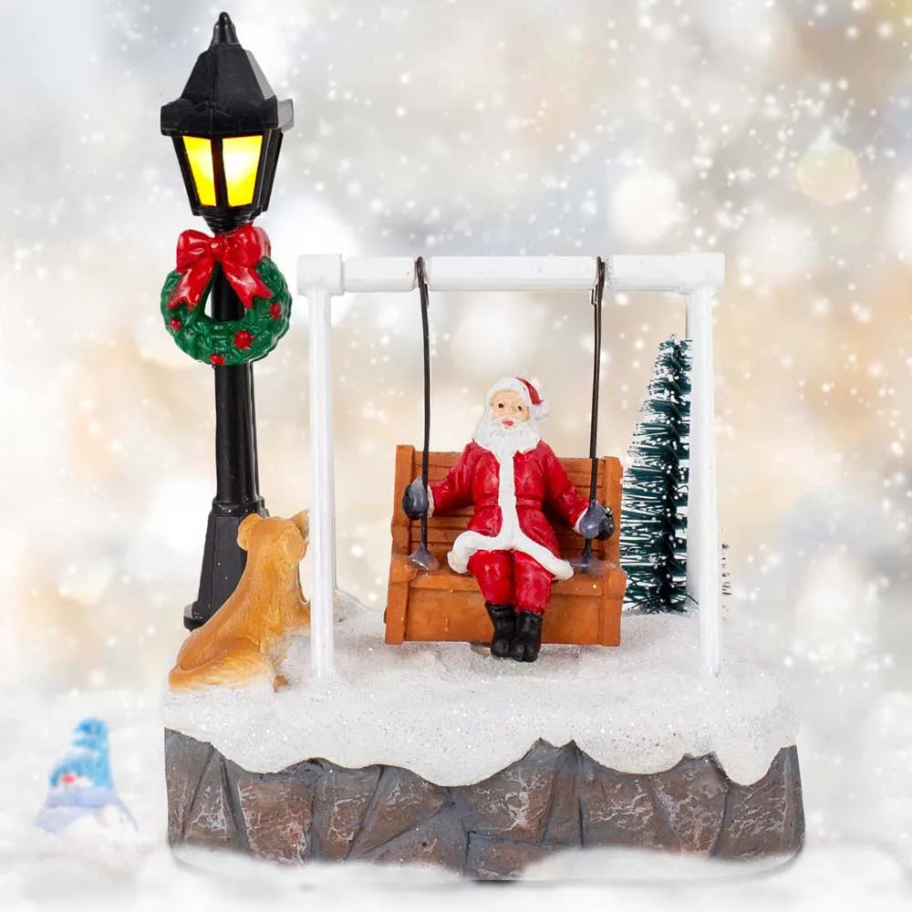 Front view of Santa swing figurine with lit lamppost, dog and Christmas tree against a snowflake background