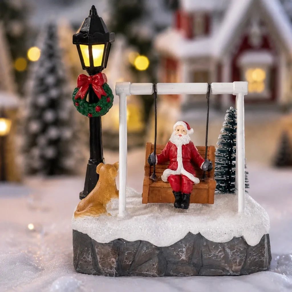 Santa swing figurine with dog, tree and lit lamppost in a snowy Christmas village setting