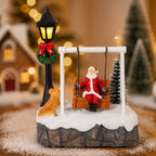 Santa Swing Christmas Scene displayed on a wooden surface with snow and warm village houses behind