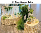 Serpentine Event Display Table cream-draped reception display with drink dispensers, white flowers and greenery.