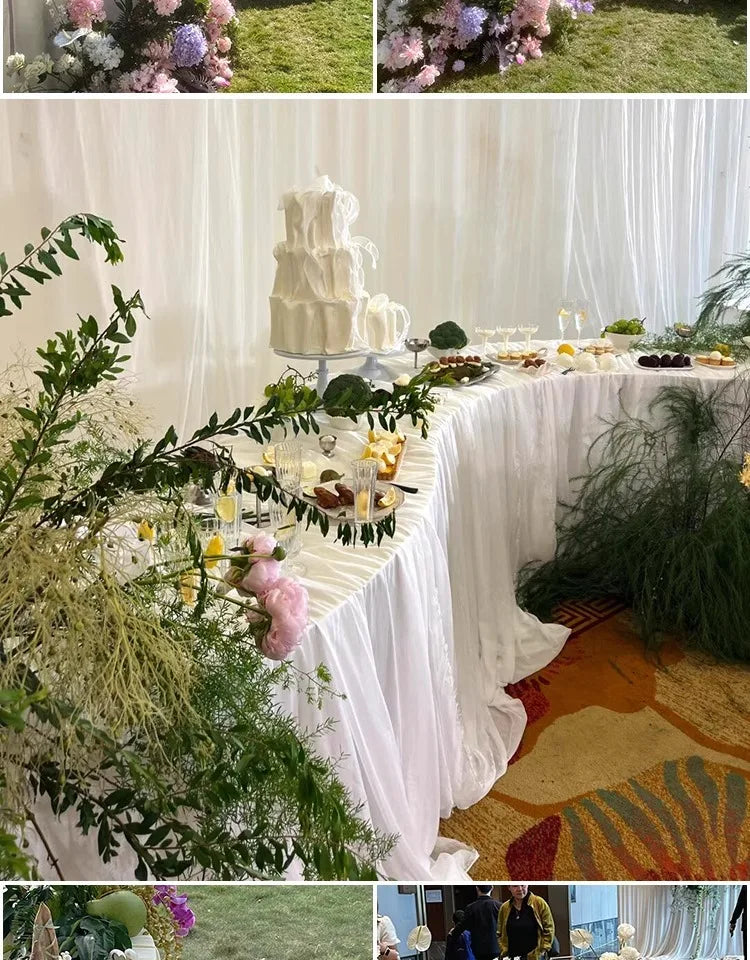 Serpentine Event Display Table white-draped curved display with a tiered cake, desserts, glassware and greenery.