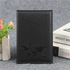 Signature Leather Passport Cover in Black, standing beside books and flowers with a tonal world-map design.