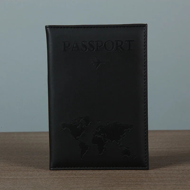 Signature Leather Passport Cover in Black standing on a wooden tabletop with tonal lettering and map details.