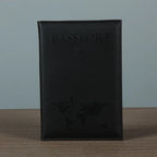 Signature Leather Passport Cover in Black standing on a wooden tabletop with tonal lettering and map details.