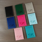 Signature Leather Passport Cover in all eight imported colors arranged face-up on a wood surface.