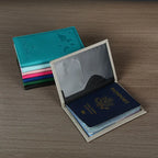 Signature Leather Passport Cover in Gray opened with a passport inside, beside a stack of colored covers.