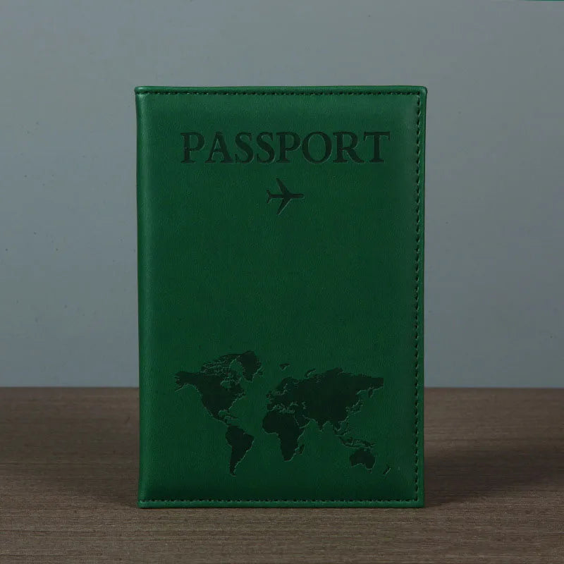 Signature Leather Passport Cover in Green standing on a wooden tabletop with its world-map front visible.