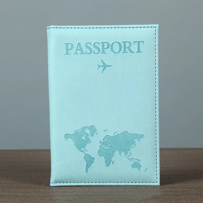 Signature Leather Passport Cover in Light Blue standing on a wooden tabletop against a plain gray background.