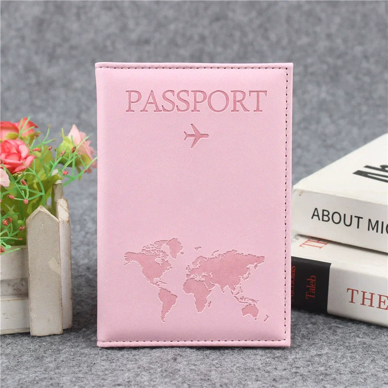 Signature Leather Passport Cover in Light Pink, standing beside books and flowers with its world-map front visible.