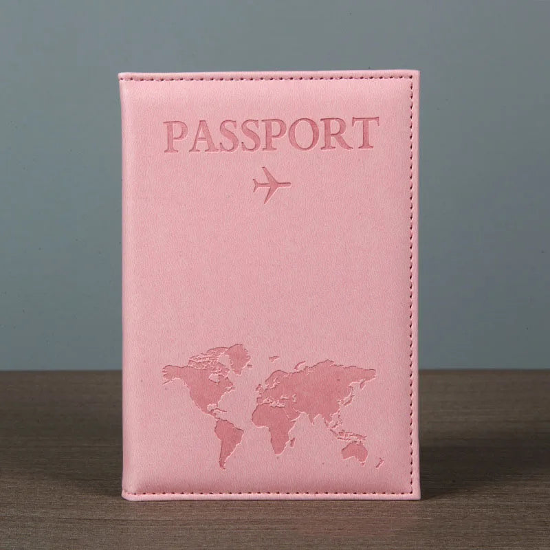 Signature Leather Passport Cover in Light Pink standing on a wooden tabletop against a plain gray background.