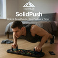 HighPeak SolidPush™ Push-Up Board in black with color-coded grips, man exercising in a home gym setting.