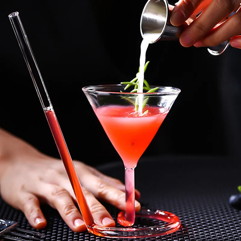 Spiral Straw Cocktail Glass with a red drink while a hand pours an ingredient into the bowl