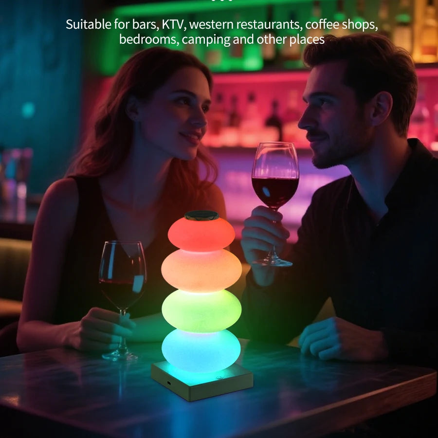 Stacked Pebble RGB Lamp glowing in four colors on a bar table between two adults.