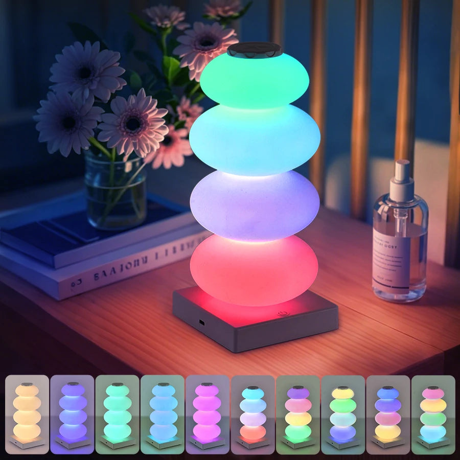 Stacked Pebble RGB Lamp on a wooden nightstand above a strip of ten color examples.