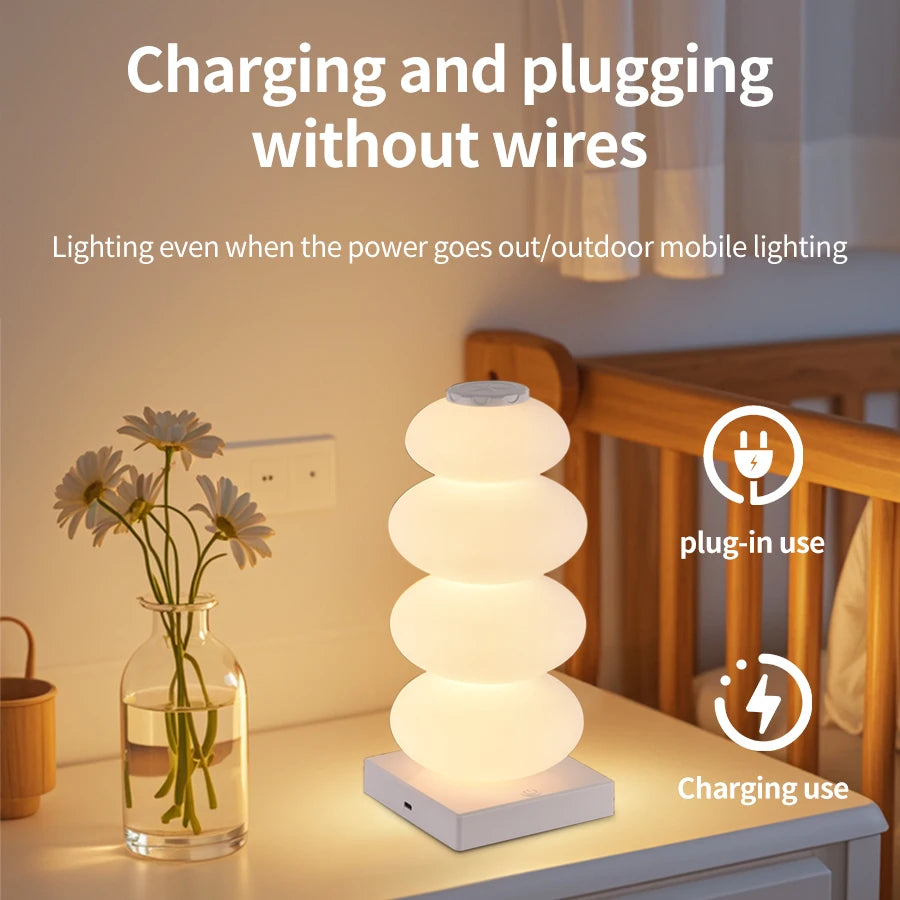 Stacked Pebble RGB Lamp glowing warm white beside flowers with charging-use graphics.