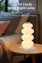 Stacked Pebble RGB Lamp glowing warm white on a round table beside a sofa.