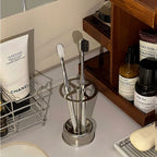 Stainless Toothbrush Holder with two toothbrushes standing on a bathroom counter beside toiletries