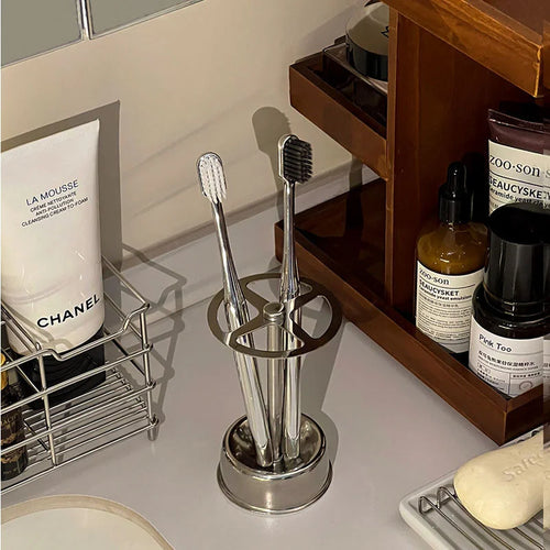 Stainless Toothbrush Holder with two toothbrushes standing on a bathroom counter beside toiletries