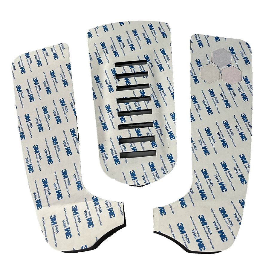 Underside of three surfboard traction pad sections showing peel-off adhesive backing and center slots
