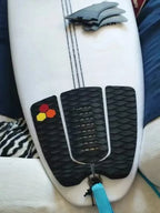 Black three-piece surfboard traction pad installed at the tail of a white board with a blue leash