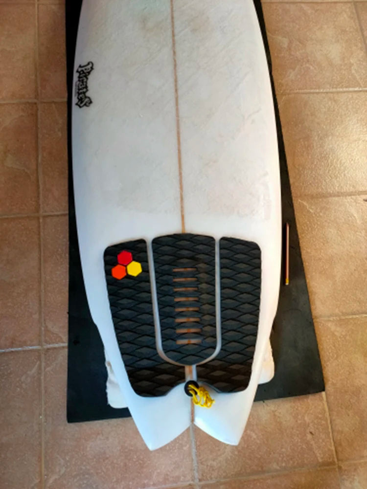 Top view of black surfboard traction pads fitted around the leash plug on a white swallowtail board