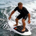 Surfer standing on a white board with a black three-piece traction pad while riding a small wave