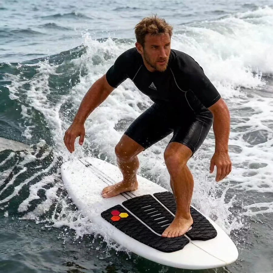Surfer standing on a white board with a black three-piece traction pad while riding a small wave
