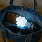 Touch Activated Bag Light — Paw shape glowing inside a denim tote beside sunglasses and a wallet.