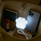 Touch Activated Bag Light — Paw shape glowing inside a handbag beside a phone and wallet.