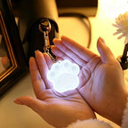 Touch Activated Bag Light — Paw shape glowing in cupped hands with its keychain clip attached.