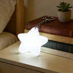 Touch Activated Bag Light — Star shape glowing beside stacked books on a bedside table.