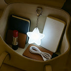 Touch Activated Bag Light — Star shape lighting a notebook and lipstick inside a tan handbag.
