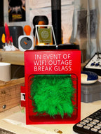 Touch Grass Meme Box upright on a desk beside a remote control and other desk accessories