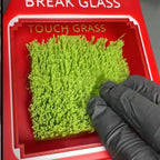Touch Grass Meme Box close-up of a gloved hand touching the green insert below the Touch Grass lettering