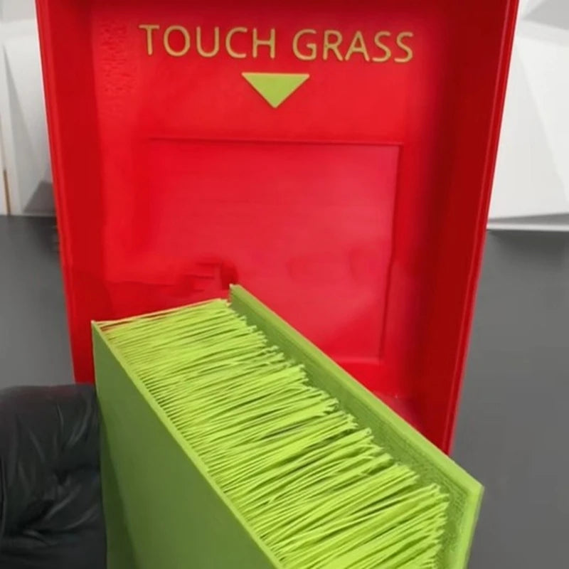 Touch Grass Meme Box with a gloved hand lifting the green grass insert from the red interior