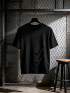 Under A Tack Tee plain black back view displayed on a hanger in an industrial setting