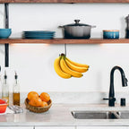 Under-Cabinet Banana Hook holding bananas beneath an open kitchen shelf near a sink and fruit basket