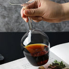Hand holding Upside Down Wine Glass by the stem with a dark drink in the lower bowl
