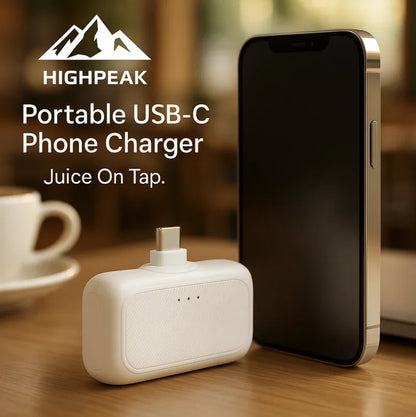HighPeak Portable USB-C Phone Charger in white next to a black smartphone on a wooden table, fast charging power bank.