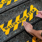 Watch Your Step Decals close-up showing hands aligning a warning strip on a stone staircase