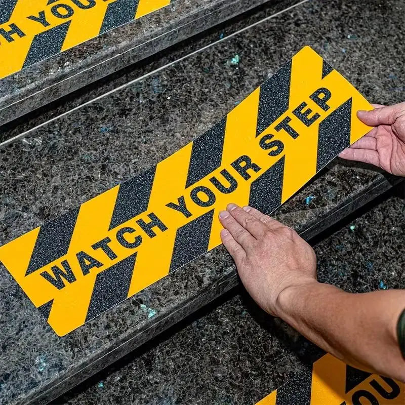 Watch Your Step Decals close-up showing hands aligning a warning strip on a stone staircase