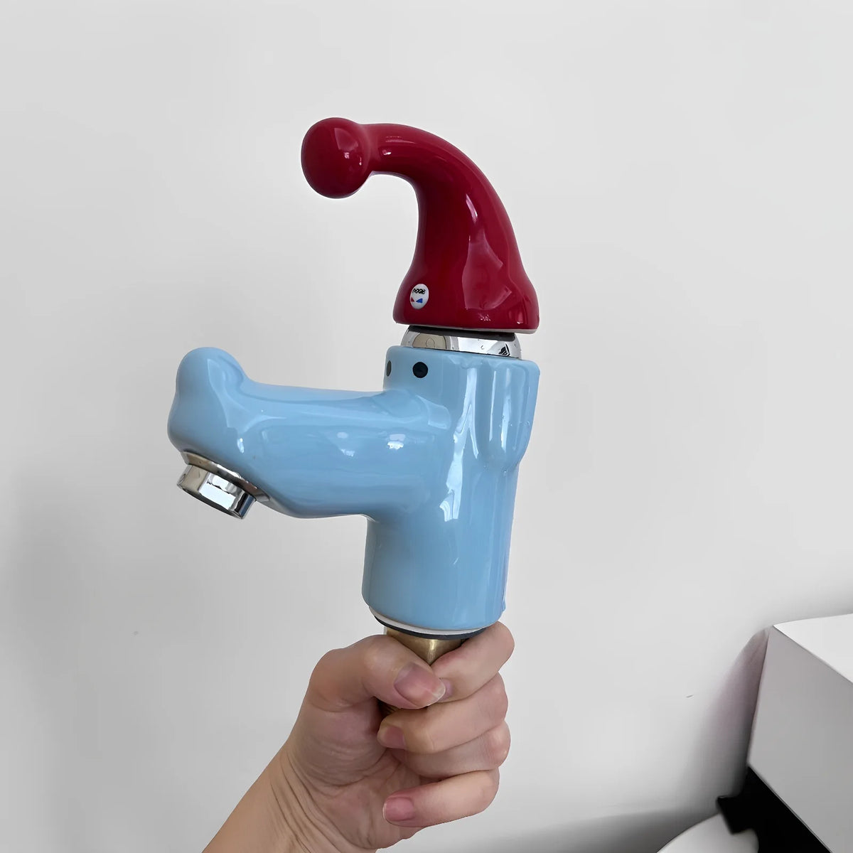 Wiggly Hat Sink Faucet handheld profile showing the glossy blue body, nose-shaped spout, and metal outlet.