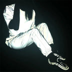 Women’s Reflective Joggers reflecting light in a seated outfit pose with bent knees and black sneakers