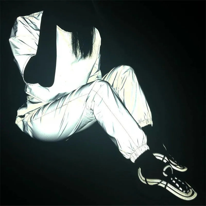 Women’s Reflective Joggers reflecting light in a seated outfit pose with bent knees and black sneakers