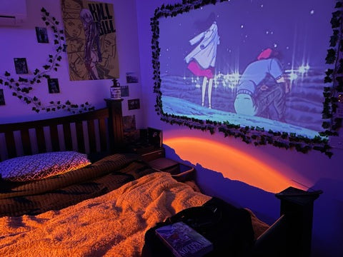 HighPeak MiniProjector displaying animated movie scene on bedroom wall with purple ambient lighting and cozy bed setup
